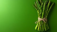 Fresh green asparagus bunch tied with twine on vibrant green background with copy space, minimalist food photography composition for healthy eating concept.