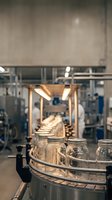 Glass jars moving on industrial conveyor belt in modern manufacturing facility with automated production line equipment and machinery.