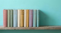 Row of colorful vintage books arranged on wooden shelf against turquoise wall for home decor, education, reading and library concepts.