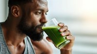 African American man drinking green smoothie in athletic wear, focused on health and wellness during morning routine.