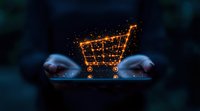 Glowing orange shopping cart icon with sparkles reflected on digital device screen in dark environment, symbolizing online retail and e-commerce technology.