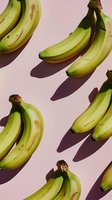 Fresh green bananas arranged in diagonal pattern casting long shadows on pink background, minimalist food photography composition for healthy lifestyle concept.