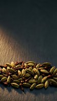 Scattered green cardamom pods and red peppercorns arranged on dark slate surface with warm golden light, suitable for culinary, food styling, and spice-related design projects.