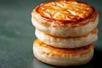 Stacked golden brown puff pastry with caramel glaze on dark green background, flaky layers and decorative pattern on top create appetizing dessert.