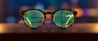 Stylish eyeglasses with green-tinted lenses reflecting digital code and data streams, representing cybersecurity, programming, and modern technology concepts.