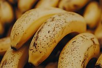 Fresh ripe bananas with natural brown spots on yellow peel in warm lighting, macro food photography showing texture and detail of tropical fruit.