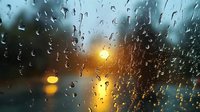 Raindrops on window glass at sunset creating atmospheric mood with blurred city lights in background during evening storm.