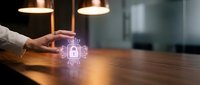 Businessman hand protecting glowing AI chip icon on wooden desk in modern office with warm lighting for technology and innovation concepts.
