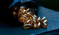 Golden vitamin capsules spilling from dark bottle onto blue textured surface in dramatic lighting, omega-3 fish oil supplements for health and wellness concept.