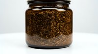 Ground coffee beans in amber glass jar with black lid on white background isolated for packaging design and culinary projects.