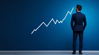 Businessman in navy suit looking at growing chart line on blue wall, rear view. Success and financial growth concept for business presentations.