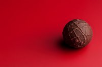 Luxury dark chocolate truffle with elegant golden drizzle on vibrant red background, perfect for confectionery and holiday food styling.