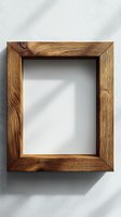 Rustic wooden picture frame on white wall with natural sunlight shadow casting geometric shapes, empty space for artwork or photography display.