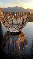 Elegant crystal bowl with intricate cut patterns reflecting golden sunset light on wet surface with mountain landscape background for luxury dining decor.