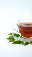 Clear glass teacup with hot tea and fresh green leaves on white background for wellness and beverage concepts.