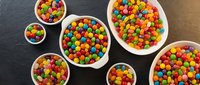 Colorful candy-coated chocolates in white bowls arranged on dark slate surface, perfect for confectionery marketing and sweet treat designs.