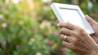 Senior woman holding tablet outdoors in garden with blurred green foliage background, technology and nature lifestyle concept for web and print.
