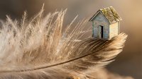 Miniature wooden house sitting on soft feather with dried grass creating dreamy home concept for real estate and property investment themes.