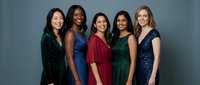 Five diverse professional women in elegant evening dresses standing together against blue background, representing teamwork, success and corporate diversity.