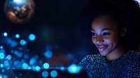 Young African American woman smiling in dark environment with magical blue bokeh lights and glitter effect creating dreamy atmospheric mood for creative portrait photography.