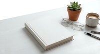 Clean minimalist workspace with blank white book, succulent plant, eyeglasses and coffee cup on white desk for productivity and organization concepts.