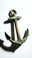Antique bronze anchor with weathered patina and verdigris finish casting shadow on white background, suitable for nautical, maritime, and vintage design projects.