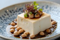 Silky tofu block garnished with mushrooms, microgreens and soy sauce on decorative blue ceramic plate, close up view of Asian cuisine appetizer.