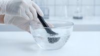 Laboratory technician in white gloves using black spoon to mix substance in glass bowl for scientific research and chemical analysis in modern lab.