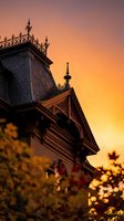 Victorian house architectural details with ornate ironwork silhouetted against dramatic orange sunset sky creating romantic historic atmosphere.