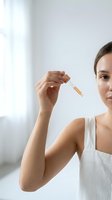 Young woman applying facial serum with dropper in bright bathroom. Natural skincare routine and beauty treatment for healthy glowing skin.