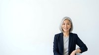 Mature woman with gray hair, Caucasian ethnicity, wearing dark blazer and light blouse, smiling confidently against white background. Professional business portrait suitable for corporate websites, leadership profiles, and business communications.