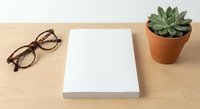 Clean workspace with blank white book, eyeglasses and succulent plant on wooden desk. Minimalist office setup for reading, writing or creative projects.