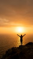 Person with raised arms celebrating freedom on cliff overlooking ocean at golden sunset. Inspirational moment of triumph and achievement by the sea.