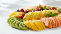 Fresh tropical fruit platter with sliced kiwi, pineapple, papaya and mixed berries arranged on white plate for healthy breakfast or dessert presentation.