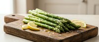 Fresh green asparagus spears with lemon slices on rustic wooden cutting board in modern kitchen. Healthy organic vegetable ingredient for cooking and meal prep.