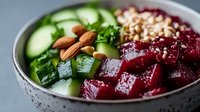 Fresh bowl with diced beets, cucumber slices, almonds, pine nuts and herbs in ceramic bowl, healthy vegetarian meal preparation on light background.