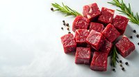 Fresh raw beef cubes with rosemary sprigs and peppercorns on light background. Premium quality meat cut into portions for cooking or grilling.