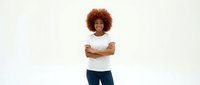 Young African American woman with curly afro hair wearing white t-shirt and jeans, arms crossed confidently on white background for design projects.