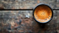 Fresh espresso with golden crema in black cup on rustic wooden background, top view with copy space for cafe menu or coffee shop promotion.