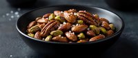 Mixed nuts and seeds in black bowl on dark surface for healthy snacking and cooking ingredients.