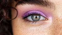 Close-up of woman's eye with vibrant purple eyeshadow makeup and freckled skin. Professional beauty cosmetics application for fashion editorial.