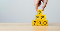 Hand placing yellow wooden blocks with AI, lightbulb, gear, magnifier, clock and question mark icons, forming a pyramid on wooden surface.