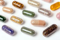 Colorful glitter-filled supplement capsules and pills scattered on white background, showcasing variety of vitamins and health supplements in decorative style.