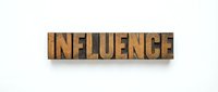 Influence word spelled in vintage wooden letterpress type blocks on white background, isolated for design use.