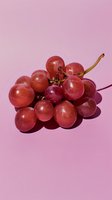 Fresh red grape cluster on pink background with harsh shadows casting dramatic contrast, minimalist food photography composition for marketing materials.