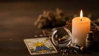 Mystical fortune telling setup with tarot cards, crystal ball, burning candle and dried herbs on dark wooden table for spiritual guidance and divination.