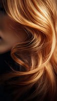 Close-up of flowing blonde hair with natural highlights and waves against dark background, showing texture and movement in warm golden tones. Suitable for beauty and haircare.