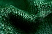 Emerald green burlap fabric with natural woven texture and wavy folds creates organic pattern with dramatic lighting and shallow depth of field.