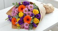 Vibrant mixed flower bouquet with roses, gerberas and chrysanthemums wrapped in kraft paper on white surface for gifting and special occasions.