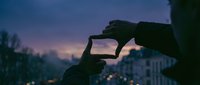 Hands framing city view at twilight with purple sky and urban lights creating artistic composition for photography and creative projects.
